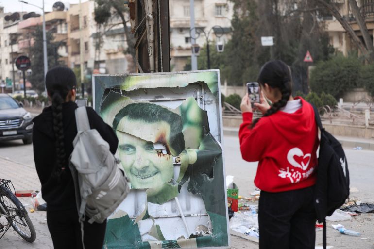 Women use their mobile phones near a damaged picture of Syrian President Bashar al-Assad as people celebrate, after Syrian rebels announced that they have ousted President Bashar al-Assad, in Qamishli, Syria December 8, 2024. REUTERS/Orhan Qereman