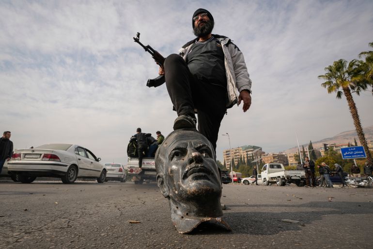 An opposition fighter steps on a broken bust of the late Syrian President Hafez Assad in Damascus, Syria, Sunday Dec. 8, 2024. (AP Photo/Hussein Malla)